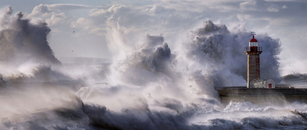 Large waves crashing beautifully into coastline with lighthouse. Mist sprays throughout.